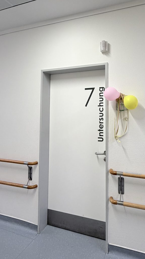 Türen haben eine große Fläche - hier wird die weiße Tür genutzt um in sehr große, kontrastreichen Buchstaben deutlich den Untersuchungsraum 7 zu kennzeichnen. Der Handlauf mit dem Hinweis in Brailleschrift endet in unmittelbarer Nähe der Klinke